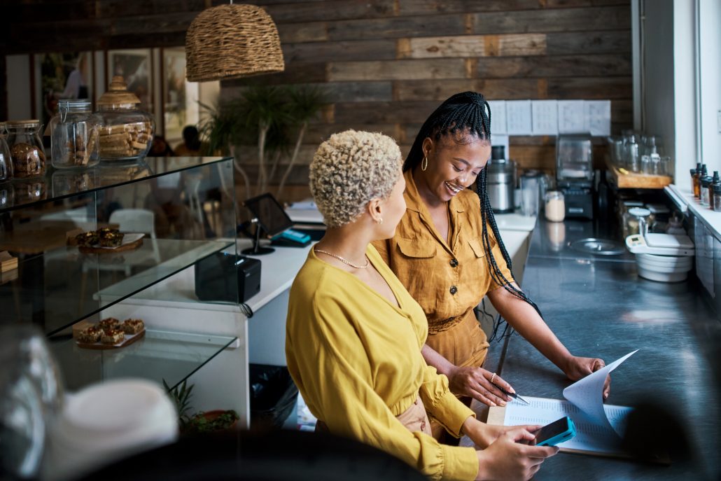 Small business owners talking and discussing the performance of their coffee shop. Black female entrepreneurs in a partnership collaborating and planning growth together inside their cafe or shop.