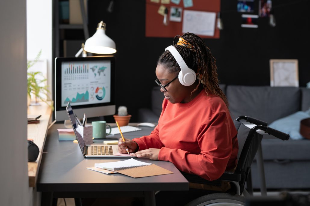 African girl in wireless headphones sitting at the table in front of the laptop and making notes, she studying at home.