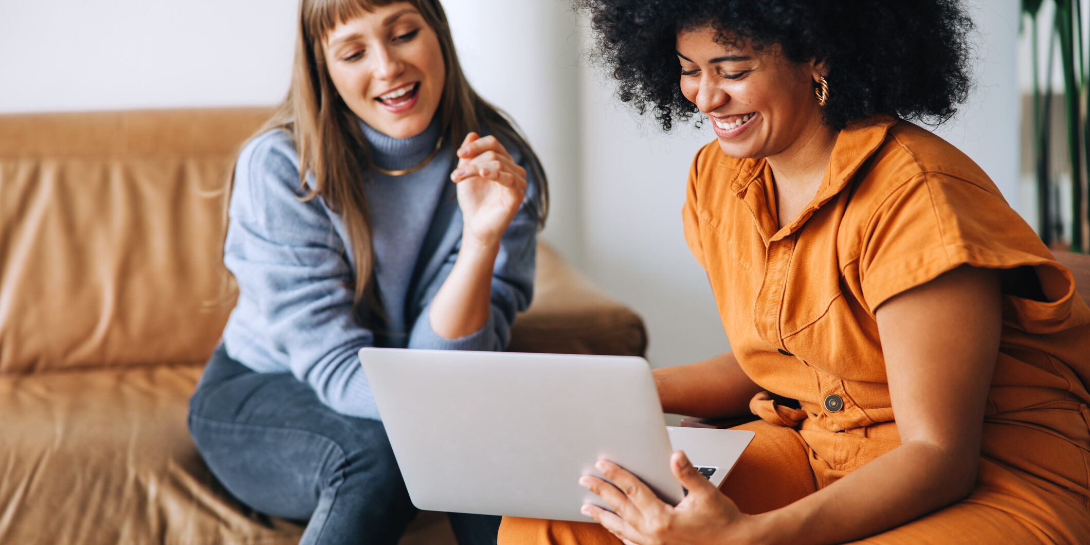 Cheerful young businesswomen smiling happily while using a laptop together. Two female entrepreneurs working as a team in a modern workplace.
