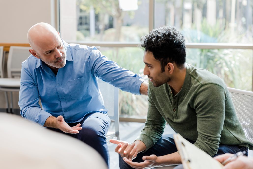 The empathetic mature adult therapist gestures and asks questions as he helps a younger man work through his problems.