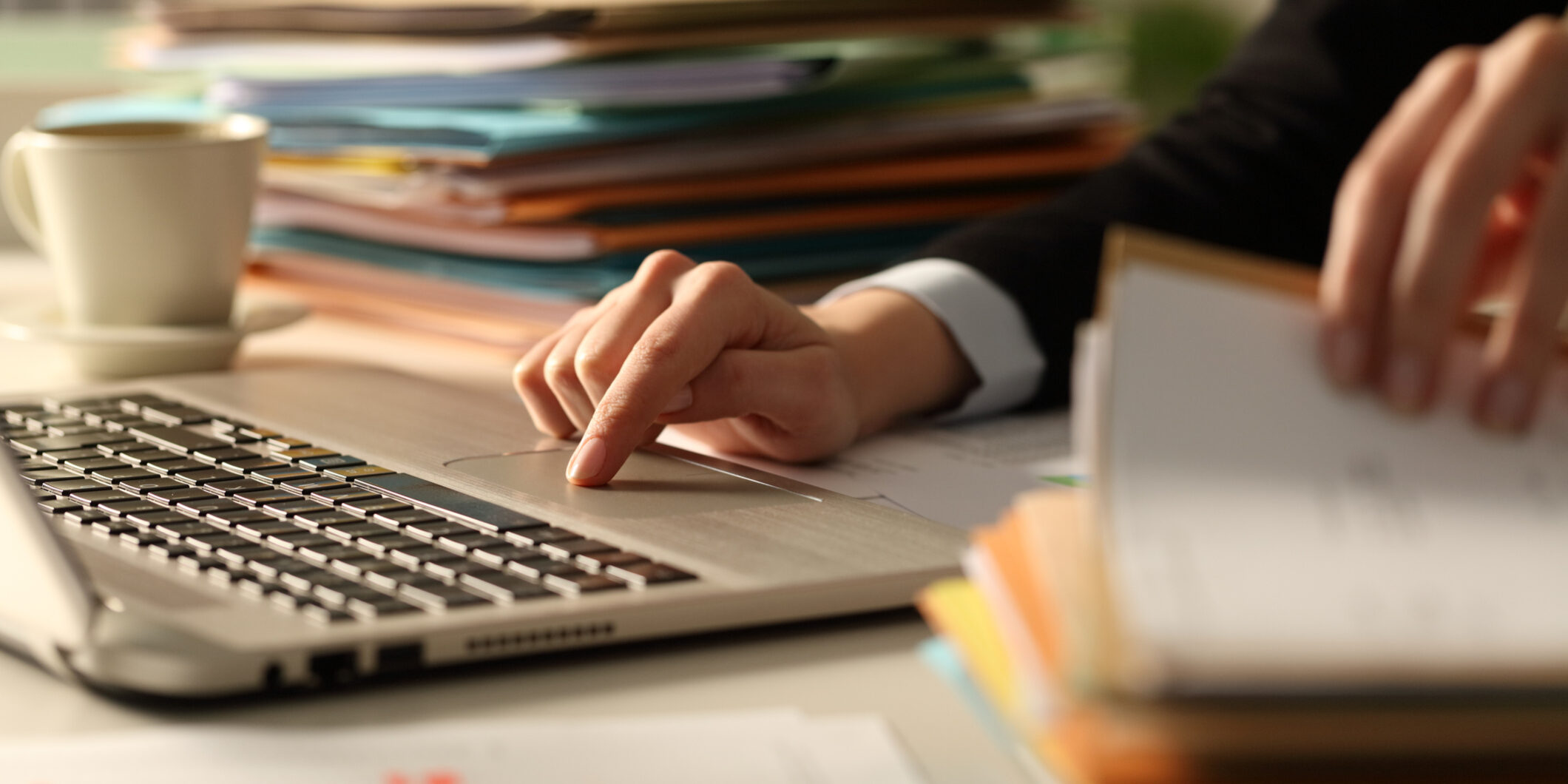 Close up of executive hands working hard late hours using laptop in the night at office checking a pile of documents