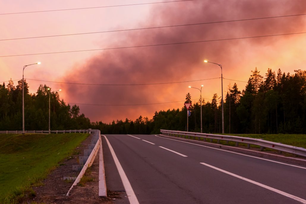 Black smoke from a fire in the crimson sky from the sunset over the road in summer