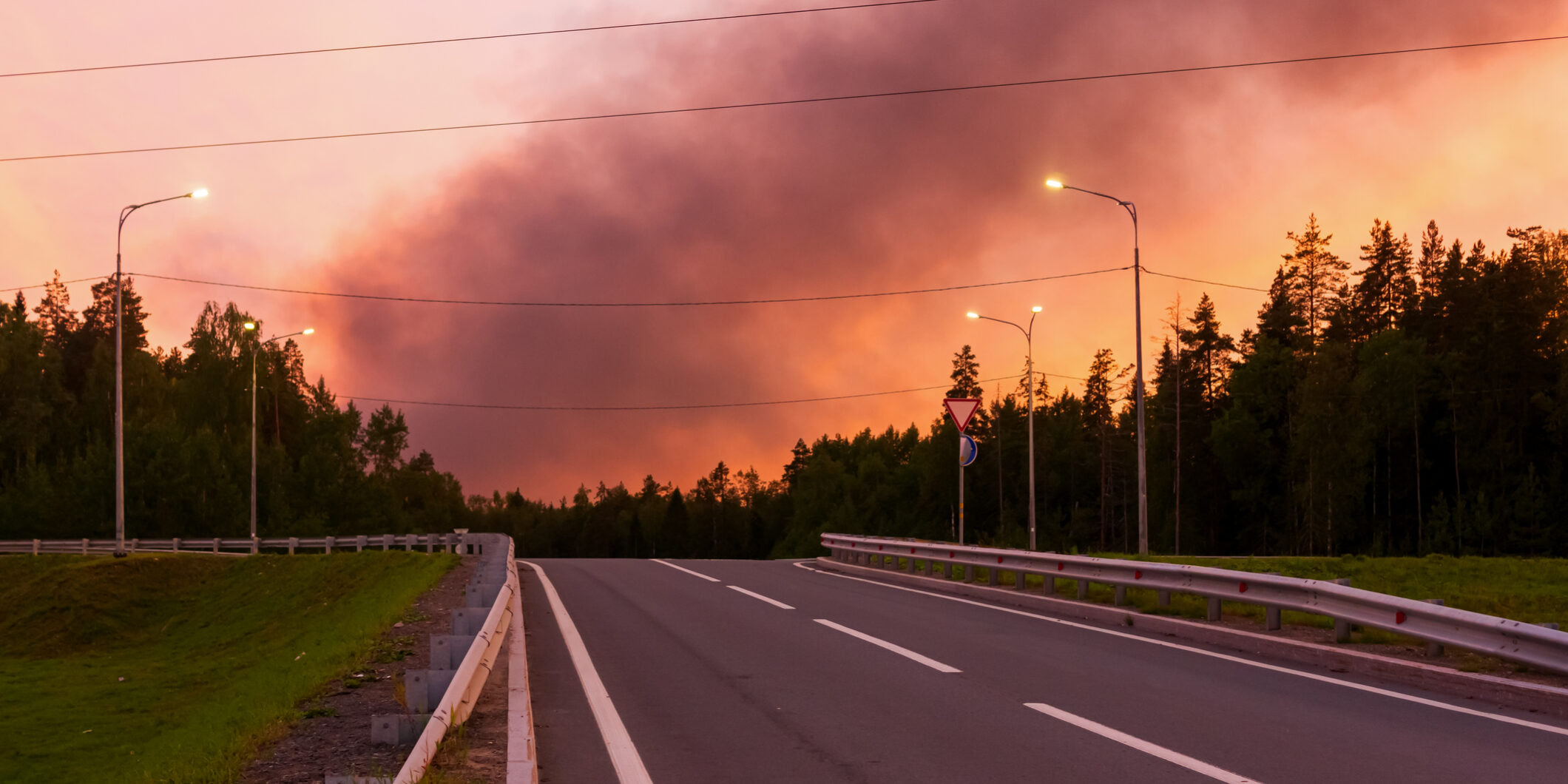 Black smoke from a fire in the crimson sky from the sunset over the road in summer