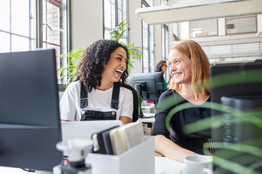 Cheerful businesswoman talking while working at desk. Happy female colleagues working together in office.