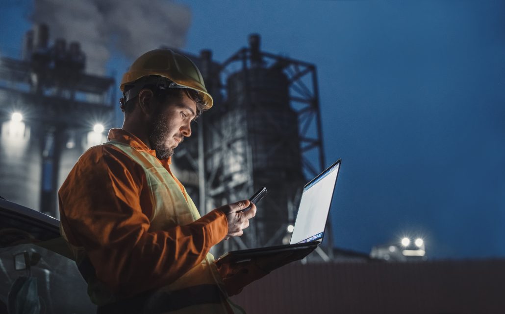 Engineer working nightshift and using technology in front of petroleum industrial factory.