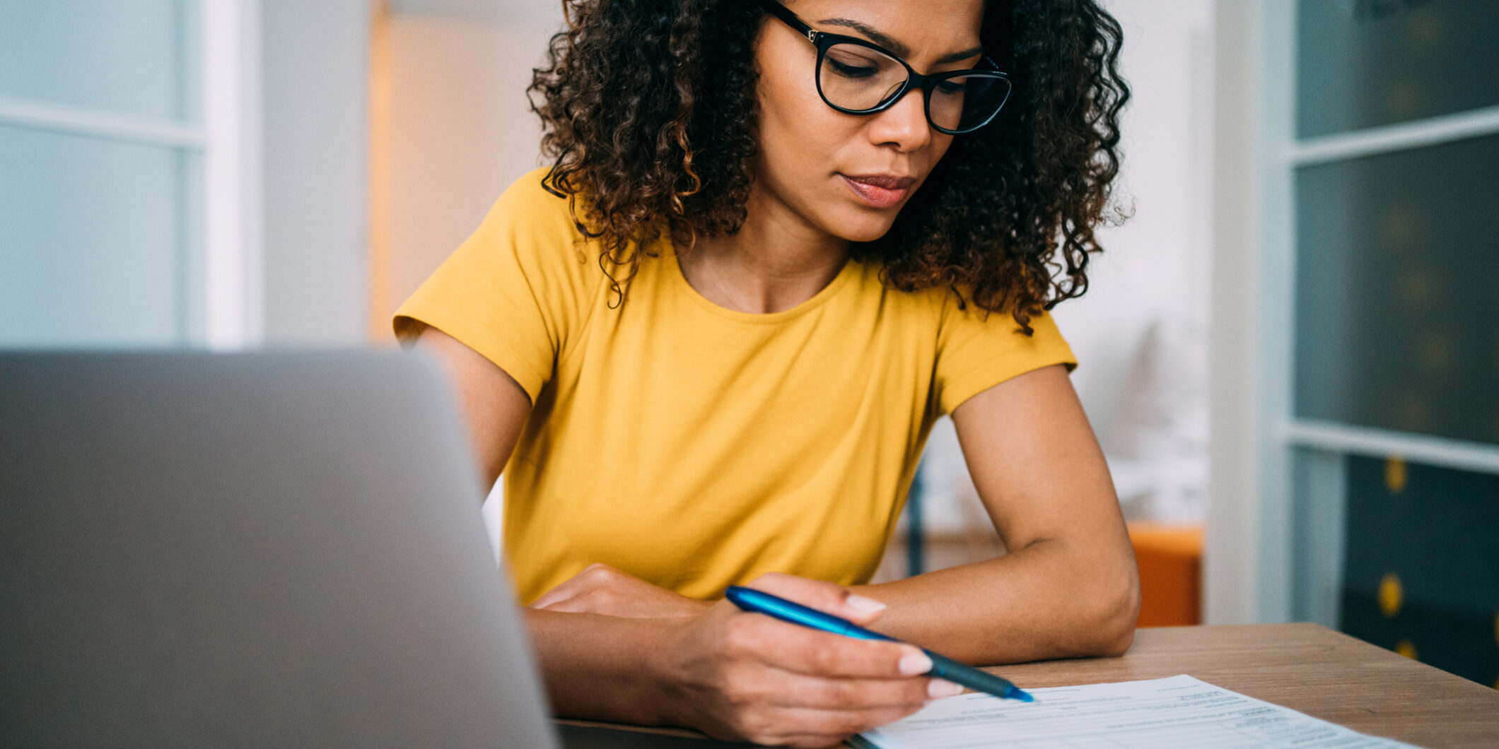 Shot of an adorable african-american businesswoman using laptop and making notes on a clipboard inside of the office.