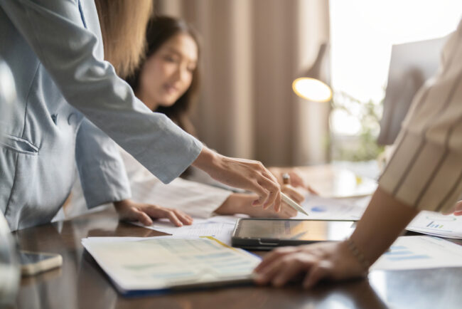 asian businesswoman brainstorm conference with her partners discussing about financial budget new project analysis with tablet and printed charts document in meeting room