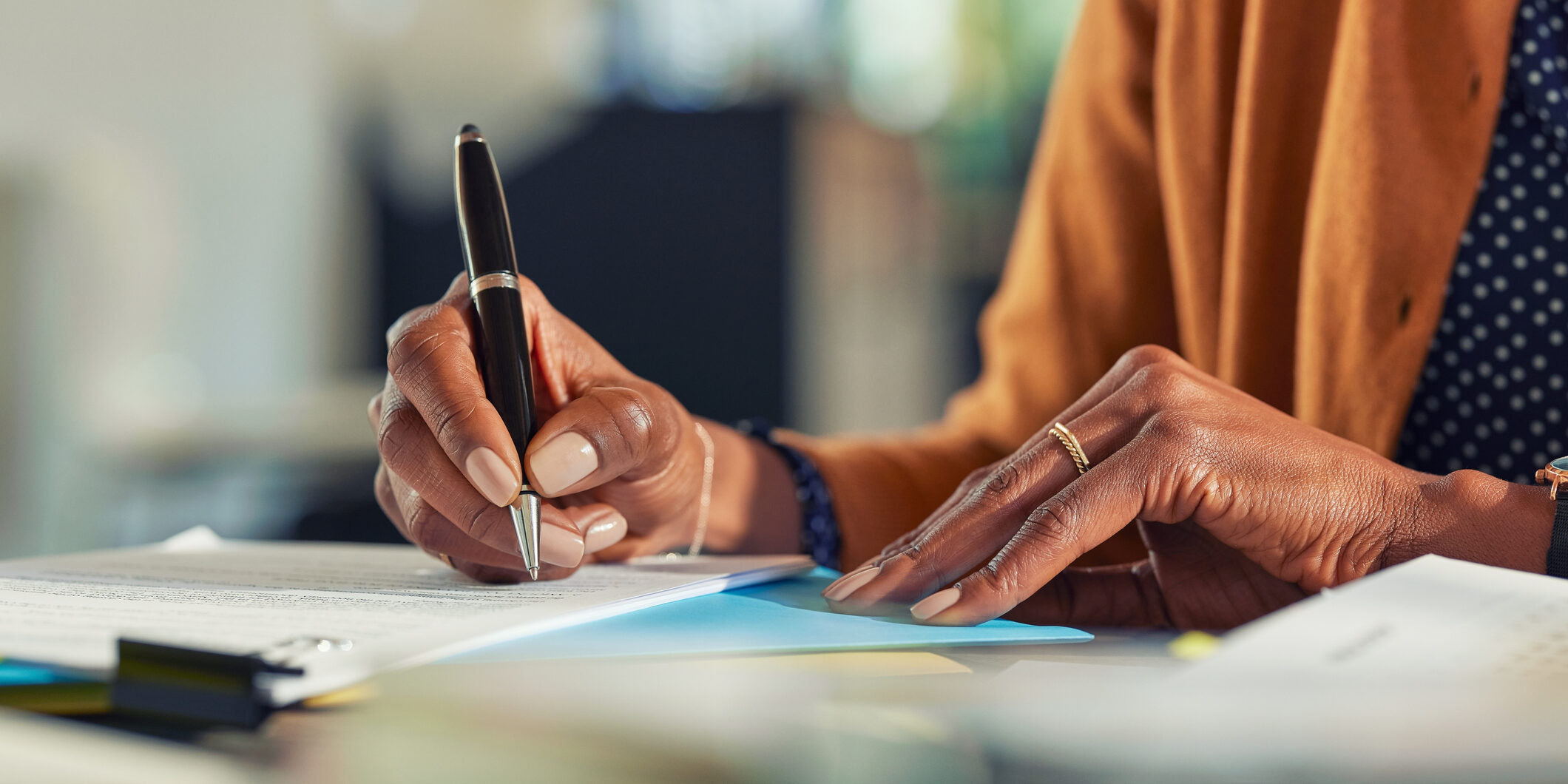 Close up of african american business woman hands writing on report while working in office. Successful black woman signing documents at home using a pen. Mid adult freelancer signing contract document on table.