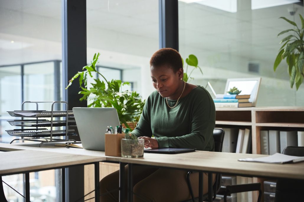 Woman, typing and laptop in a office with digital work at a desk with email at job. African female person, technology and ux designer on a website doing internet research at a company working