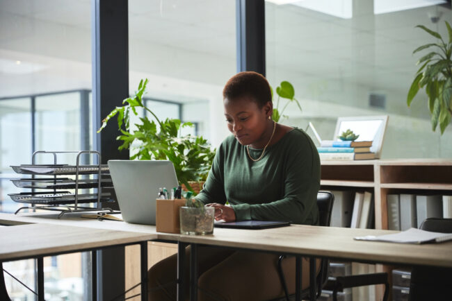 Woman, typing and laptop in a office with digital work at a desk with email at job. African female person, technology and ux designer on a website doing internet research at a company working