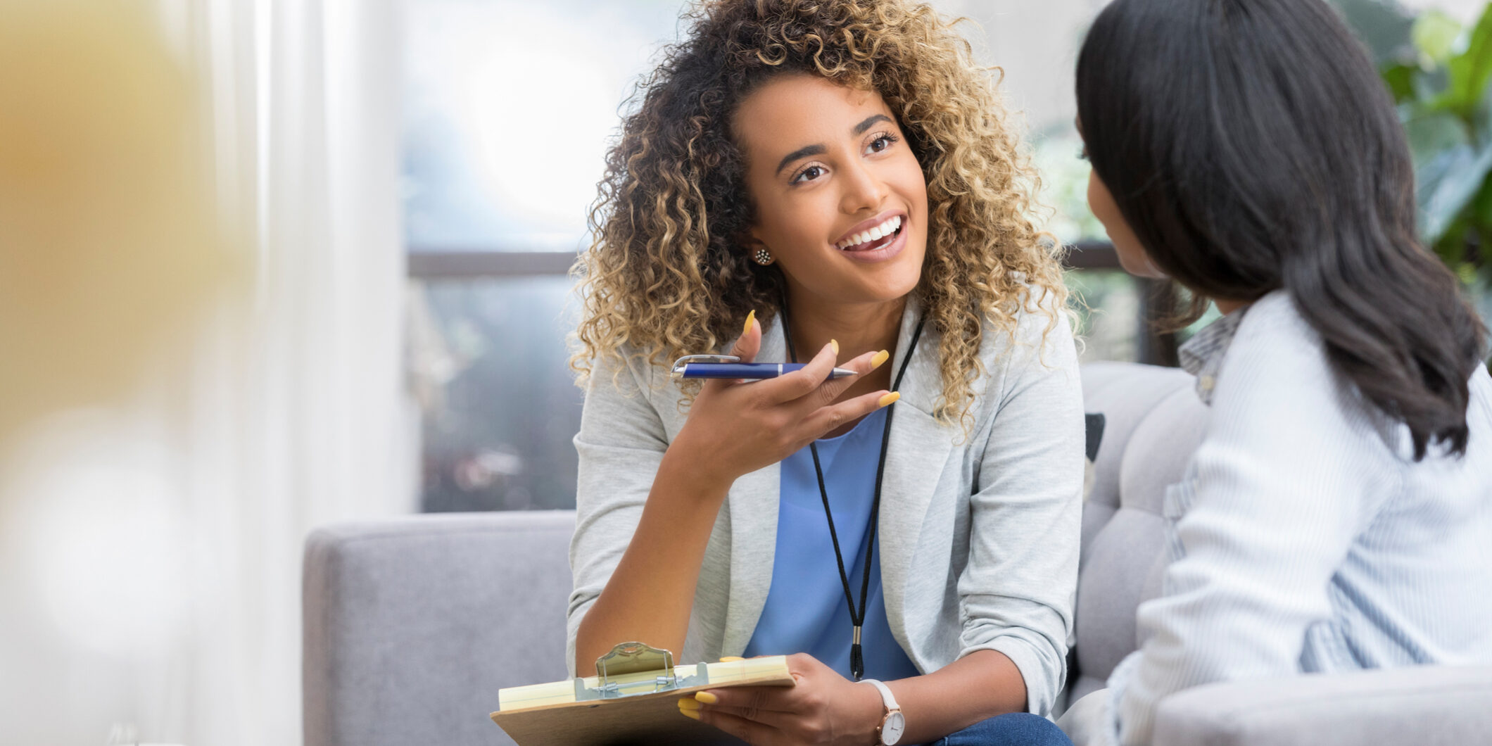 Positive young female therapist gestures as she talks with a female client. The therapist smiles warmly as she talks with the young woman.