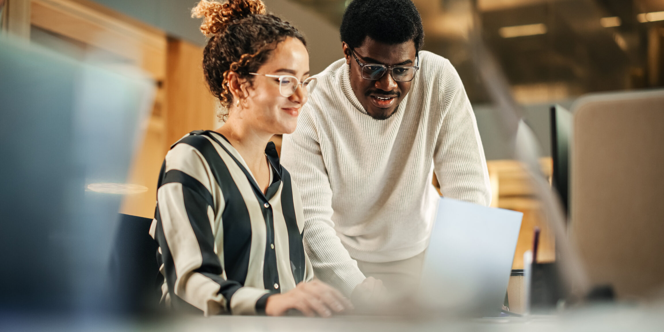 Portrait of Two Creative Colleagues Using Laptop to Discuss Work Project at Office. Young Black Technical Support Specialist Helping Female Customer Relationship Coordinator. Teamwork Concept
