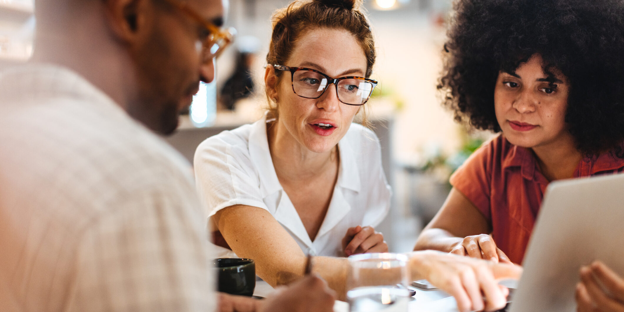 Business women having a work lunch in a café, exchanging ideas and discussing their projects with a client. Young business team using a laptop as they sit around a coffee table.