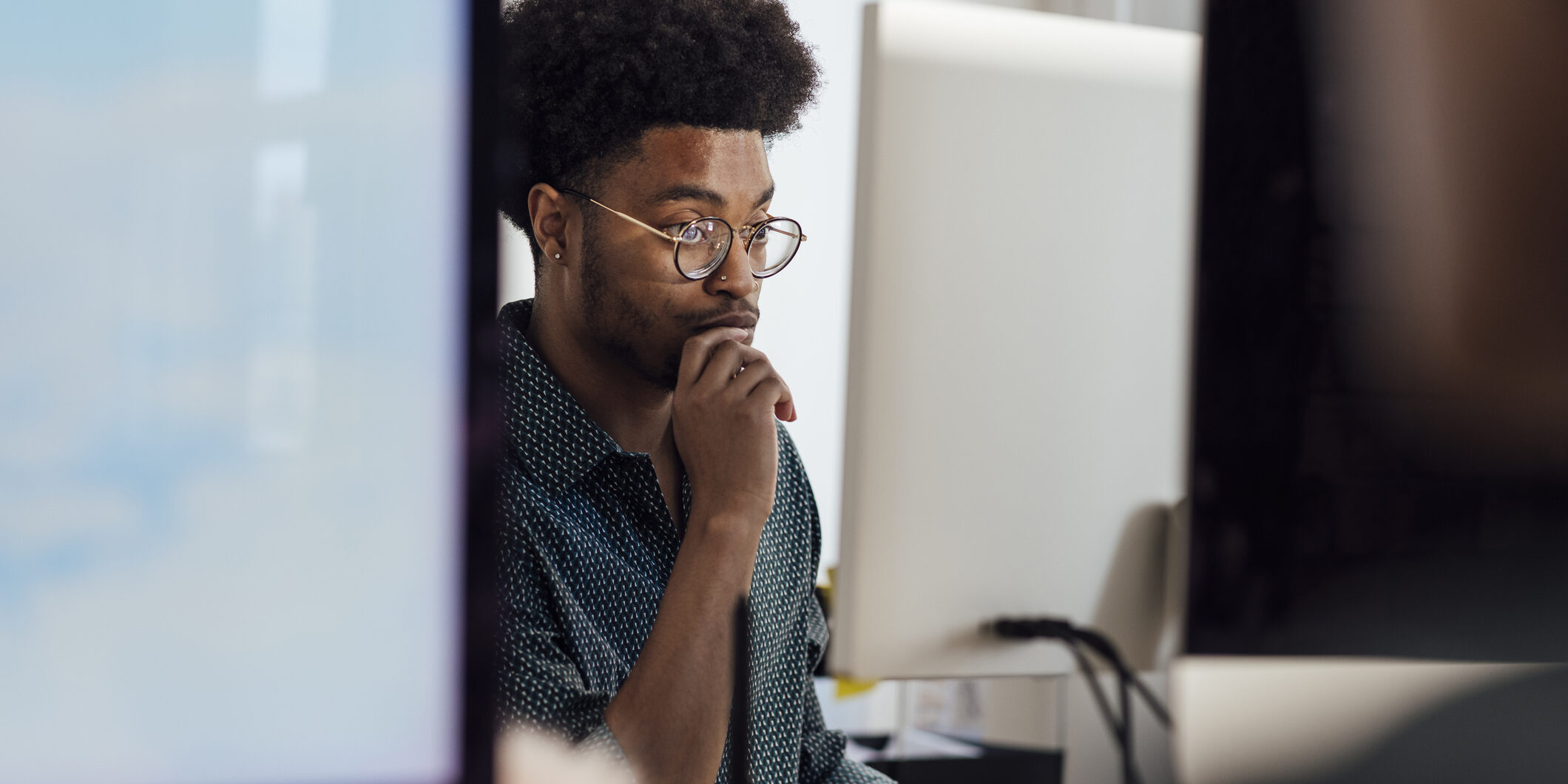 Close-up of a young male office worker sitting at her desk using a computer to complete her work in the office in Newcastle, England. He is wearing smart casual work clothing and he is working to a deadline.